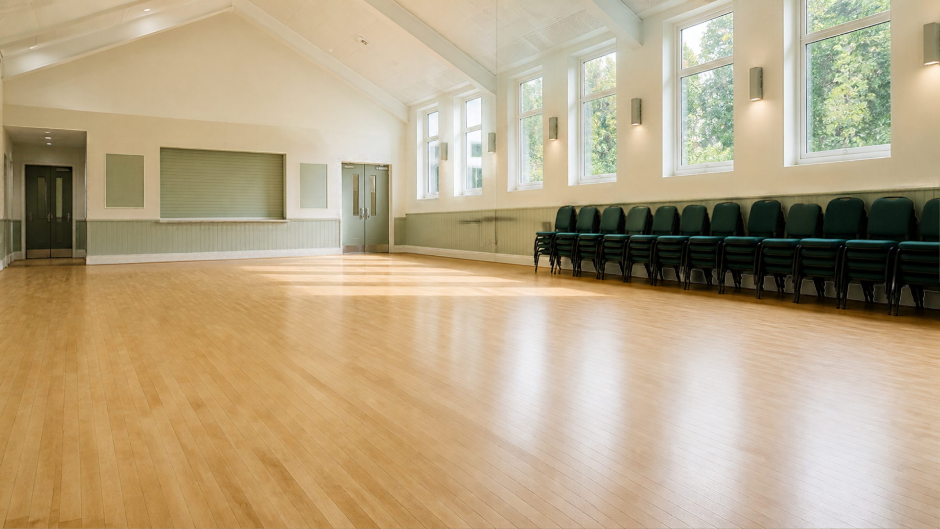 An empty community hall with a wooden floor and stacked chairs